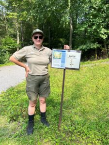 Angela, in her DCNR uniform, stands in front of a sign that has the cover of a bilingual nature book and a post with the information about Latino Conservation Week.