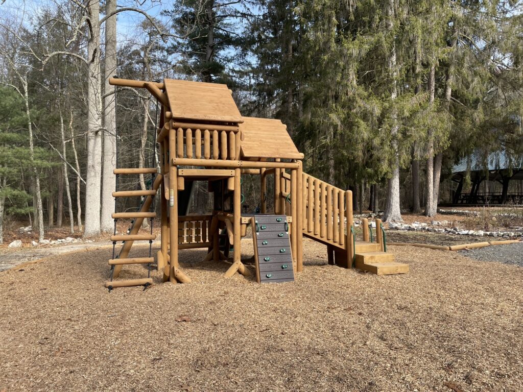 A wooden playground with green plastic slides sits in the middle of an area surrounded by woodchips at Mont Alto State Park.