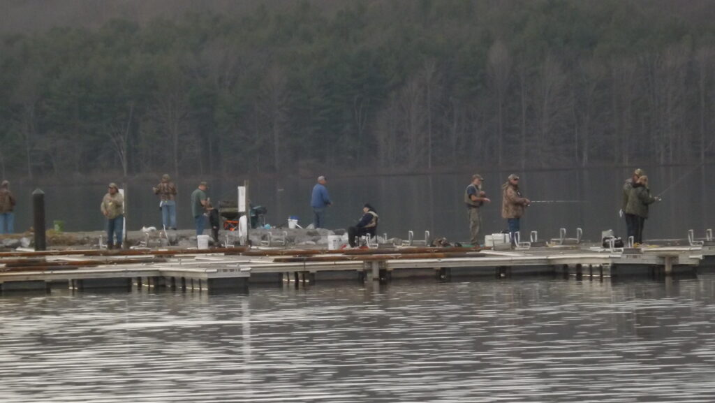 10 people, 9 men and 1 woman, scattered over a large dock fishing, most are standing